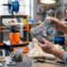 An engineer demonstrating the benefits of 3D printing by holding a complex custom mechanical prototype in a workshop.